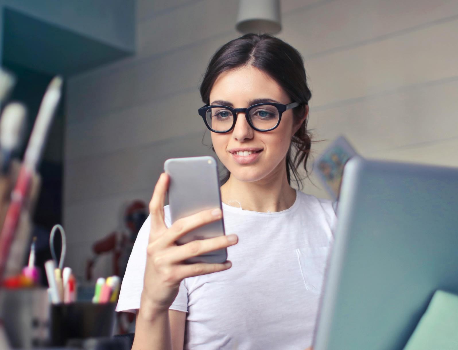 Eine junge Frau schaut freudig auf Ihr Smartphone